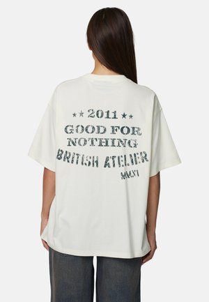 T-shirt en coton blanc avec texte imprimé. Le design comprend « 2011 GOOD FOR NOTHING » et « BRITISH ATELIER » en lettres usées. Coupe décontractée.