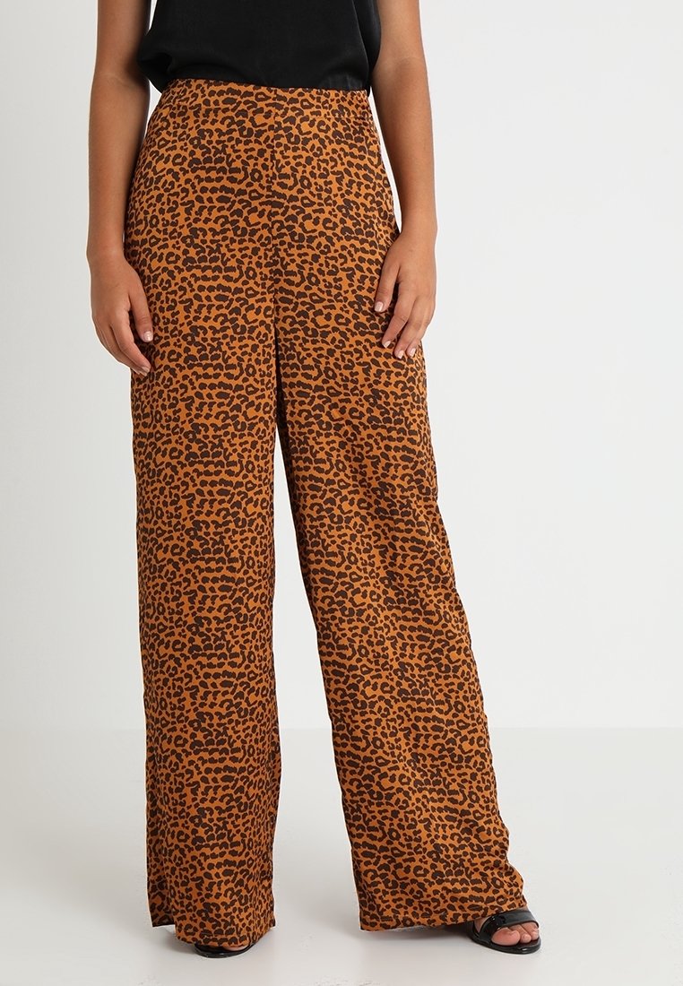 Pantalon marron à jambes larges avec imprimé léopard noir, porté avec un haut noir sans manches et des sandales noires à bout ouvert.