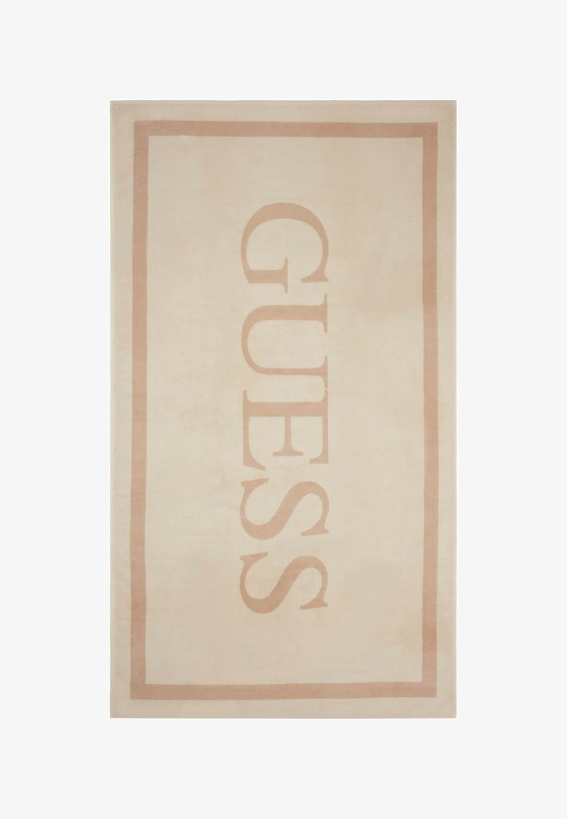 Vaalean beige matto, jossa on suuri "GUESS"-logo tummemmassa beige-värissä, jota ympäröi sopiva suorakulmainen kehys. Pehmeä rakenne.