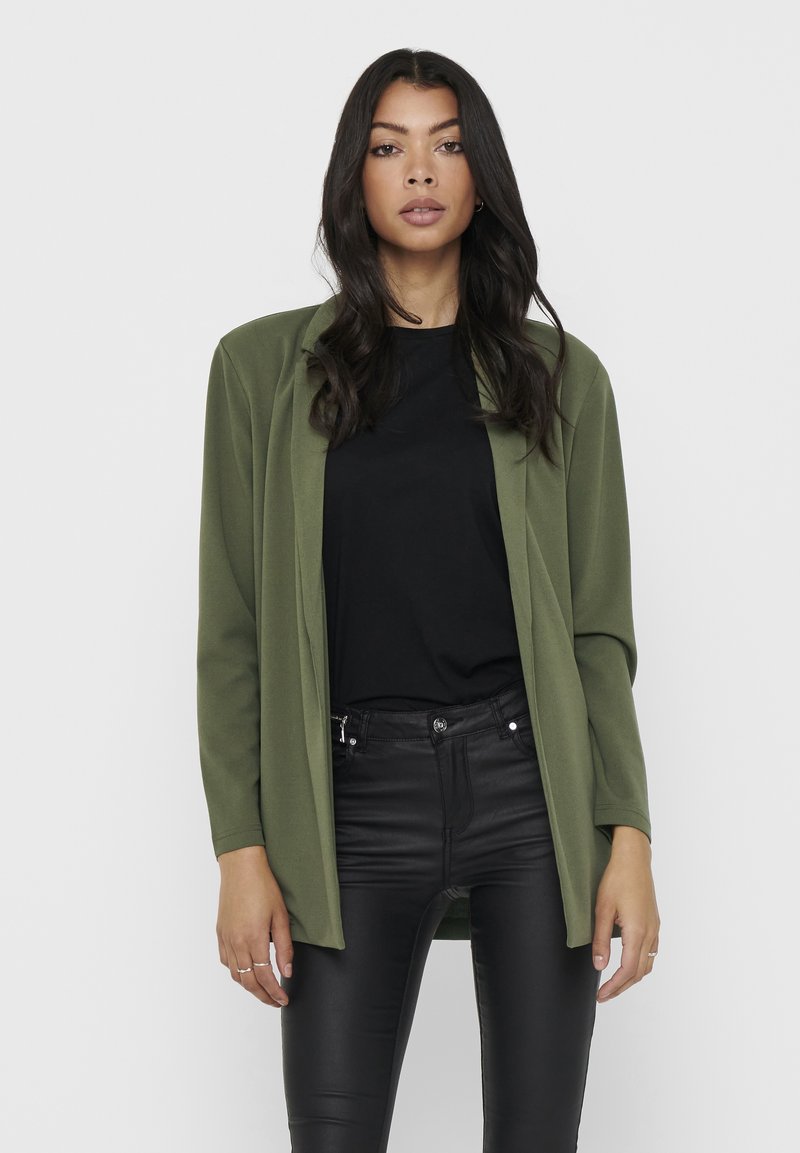 Blazer suave em verde oliva com mangas longas, design de frente aberta, sobre uma blusa preta, combinado com calças ajustadas pretas. Textura de tecido lisa.