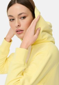 Gele hoodie gemaakt van zacht stof, met geribde boorden en een capuchon met trekkoord. Opvallend door het minimalistische ontwerp en subtiele logoaccent.