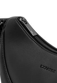 Borsa a tracolla in pelle nera con cerniera argentata, superficie testurizzata e dettaglio con logo in rilievo. Il design è elegante con bordi curvi.