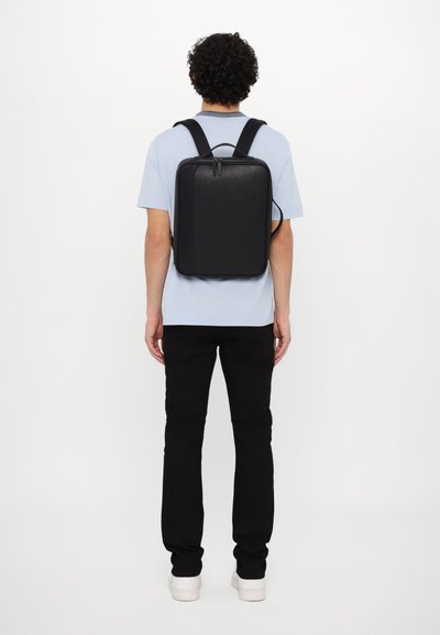 Black, rectangular backpack with a zippered closure and padded shoulder straps. Smooth texture, minimalistic design, suitable for daily use.