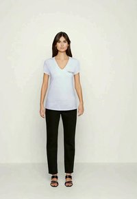 Light blue V-neck t-shirt with short sleeves, paired with black pants and black strappy sandals. Minimalistic design with embroidered detail.
