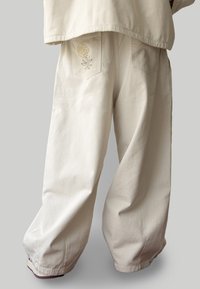 High-waisted wide-leg pants in off-white fabric, featuring a floral embroidery on the back pocket and a relaxed fit.