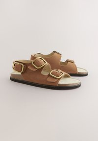 Brune ruskindsandaler med tre justerbare guldspænder, åben tå-design, formet fodseng og en tekstureret sort gummisål.