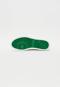 Talpa de pantof alb cu o bază din cauciuc verde texturat. Prezintă modele circulare și de valuri pentru un design cu aderență. Numele brandului este încorporat.