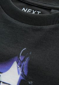 Černá mikina s vroubkovaným kulatým výstřihem a barevným grafickým designem v purpurové a bílé na přední straně. Štítek "NEXT" na límci.