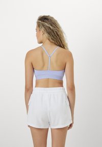 Lys lavendel sport bh med racerback-design og teksturert bånd, brukt med hvite shorts med sidelommer.
