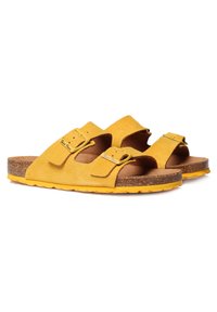 Sandali gialli in suede con doppie cinghie regolabili, plantare in sughero e suola in gomma testurizzata. Presentano un design minimalista e una forma aperta sulla punta.