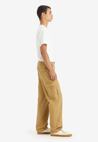 White t-shirt paired with tan cargo pants featuring multiple pockets, a loose fit, and white sneakers with textured soles.