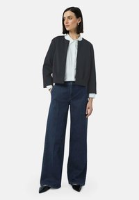 Donkergrijze cropped jas, witte coltrui en wijdvallende dark denim jeans. Jas heeft een gladde textuur; jeans hebben een klassieke pasvorm.