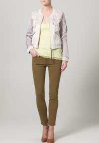 Ljusgrå bomberjacka med blommönster, tillsammans med en gul topp med spetsdetaljer, olivgröna byxor och beige klackar.