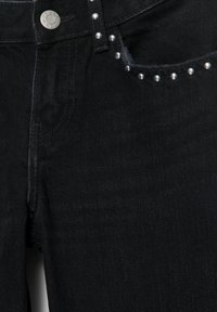 Čierne denimové džínsy so striebornými cvočkami pozdĺž prednej kapsy a pásu, s kovovou gombíkovou a klasickou päťkapsovou konštrukciou.