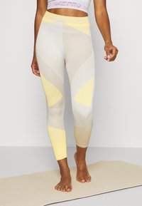 Světlé žluté a béžové sportovní legíny s geometrickým vzorem, vyrobené z pružného, texturovaného materiálu. Případný střih s vysokým pasem.