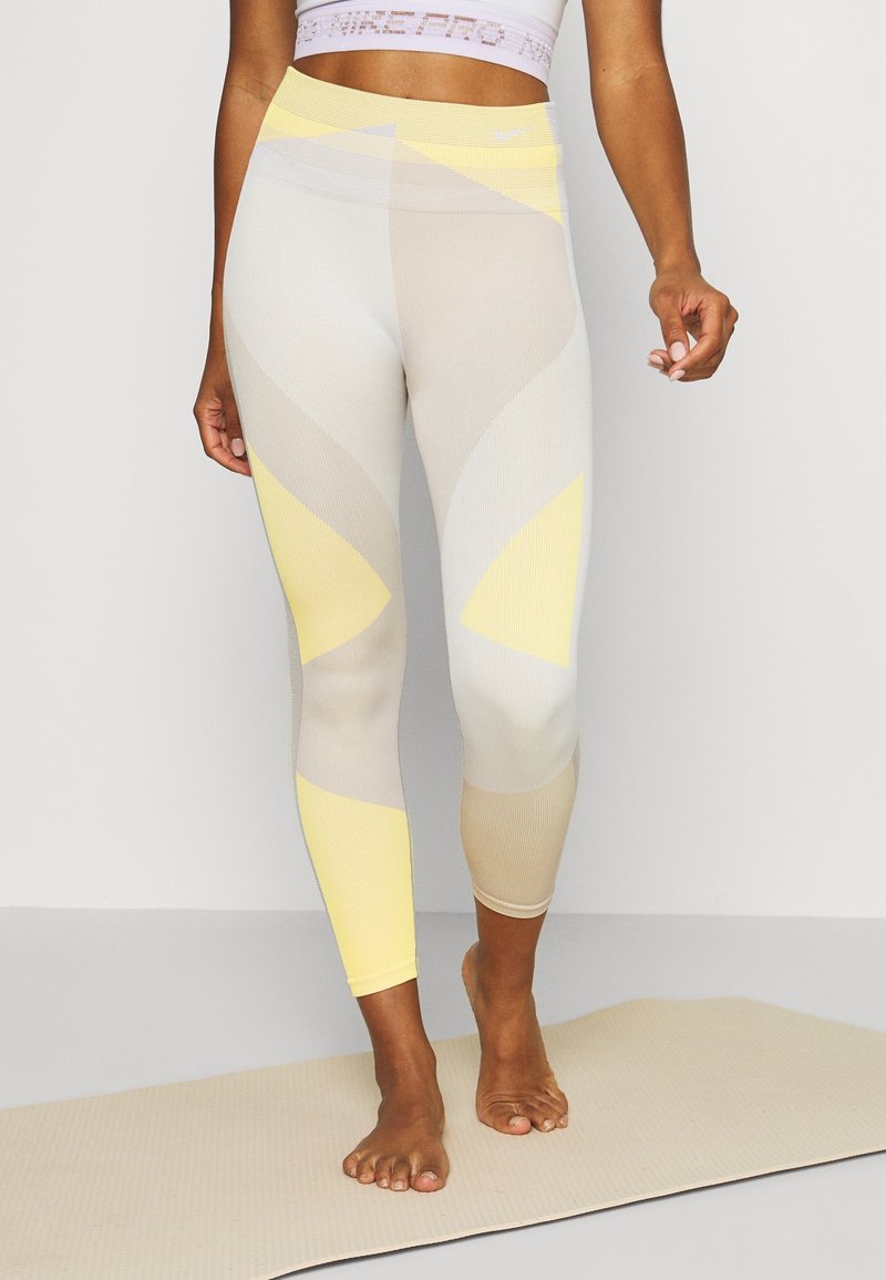 Světlé žluté a béžové sportovní legíny s geometrickým vzorem, vyrobené z pružného, texturovaného materiálu. Případný střih s vysokým pasem.