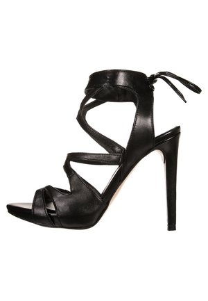 Sort højhælet sandal med krydsede læderstropper, åben tå og bindebånd om anklen. Har et slankt design og tekstureret overflade.