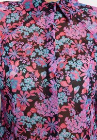 Blusa floral con fondo negro y vibrantes patrones de flores en rosa y azul, con cuello y cierre de botones en la parte delantera.