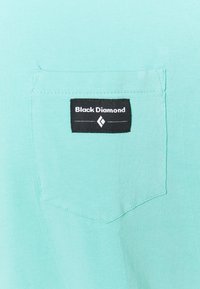 Světle modrá látková kapsa s černou obdélníkovou nálepkou, na které je napsáno "Black Diamond", a bílým diamatovým logem pod textem.
