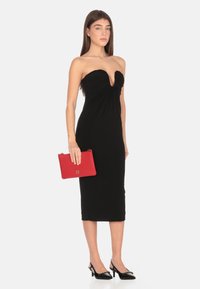 Abito nero senza spalline con scollatura a V profonda e texture arricciata. Abbinato a una pochette rossa e tacchi a slingback neri.