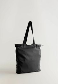 Melnā auduma soma ar izturīgām melnām siksnām un augšā rāvējslēdzēju, plaša kvadrātveida forma un gluda tekstūra.