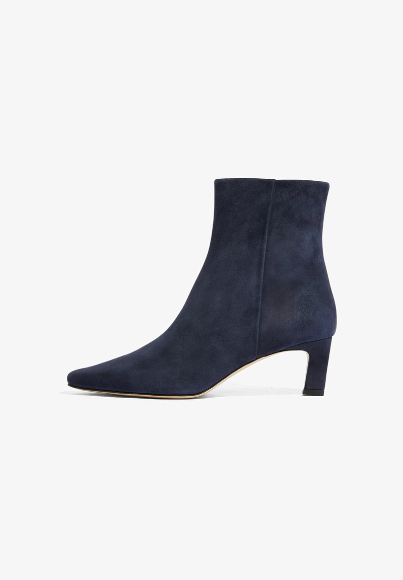 Mornarsko plava suđena gležnjača s uskim vrhom i kratkom blok petom. Ima glatku teksturu i minimalistički dizajn.