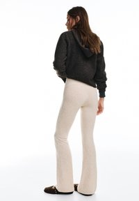 Sötétszürke kapucnis pulóver világos bézs, bővülő szárú nadrággal párosítva. Az anyag puha és texturált hatású. A modellen barna lábbeli látható.