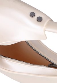 Crème synthetische handtas met een gladde afwerking, voorzien van twee metalen drukknoopjes en een contrasterende rits langs de opening. De binnenkant is bruin.