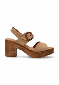 Sandalia de ante beige con una tira ancha en los dedos, hebilla ajustable en el tobillo y un tacón grueso con textura de madera. La suela de plataforma mejora la estabilidad.