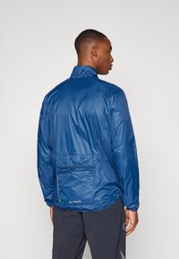 Navy blue lightweight jacket featuring a high collar, elastic cuffs, and a back pocket. Made from glossy, water-resistant material.