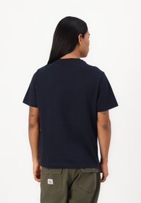 T-shirt in cotone blu navy con maniche corte e collo a girocollo, caratterizzato da un design semplice sulla parte posteriore. Indossato con pantaloni cargo verde oliva.