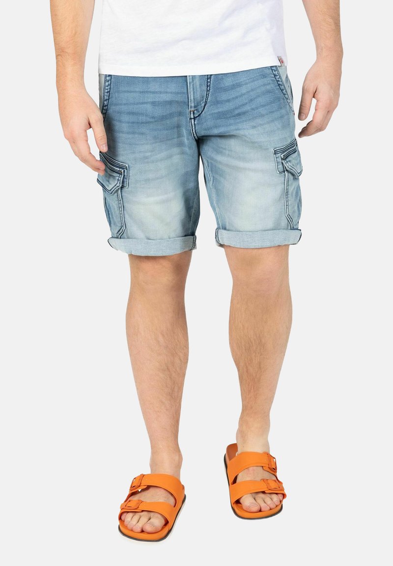 Light blue denim cargo shorts with rolled cuffs and side pockets, paired with orange sandals featuring a double strap and buckle detail.