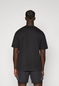 Sort kortærmet t-shirt med rund hals, lavet af bomuld, med en glat tekstur og en afslappet pasform, vist fra ryggen.