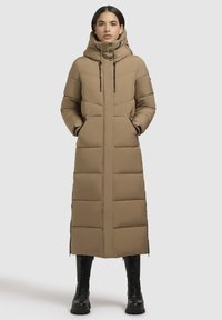 Cappotto imbottito lungo beige con cappuccio, caratterizzato da una trapuntatura verticale, tasche laterali e dettagli in zip nera. Tessuto testurizzato e vestibilità casual.