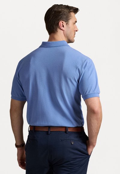 Svijetloplava polo majica s kragnom i kratkim rukavima, teksturirana tkanina, u kombinaciji s tamnoplave hlače i smeđim kožnim remenom.