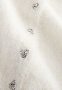 Il tessuto bianco e soffice presenta tre strass argentati decorativi con una superficie texturizzata, disposti a grappolo sul materiale.