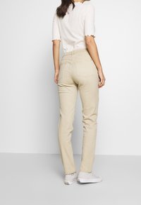 Vaqueros skinny beige de tiro medio, con cinco bolsillos y una textura suave, combinados con calzado blanco y una blusa clara texturizada.
