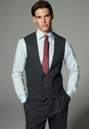 Gray double-breasted vest with a notched collar, worn over a light blue shirt and complemented by a burgundy tie with a silver tie clip.