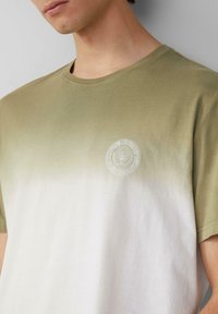 Kurzarm-T-Shirt in einem hellgrünen bis weißen Farbverlauf, aus weichem Baumwollmaterial, mit Rundhalsausschnitt und einem kleinen runden Logo auf der Brust.