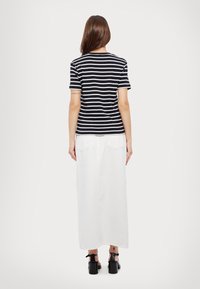 Černobíle pruhované tričko s krátkým rukávem, spárované s dlouhou bílou sukní. Oblečení doplňují černé sandály na podpatku.