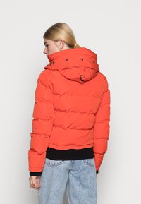 Rode gewatteerde jas met een afneembare capuchon, zwarte ribgebreide manchetten en zoom, met drukknoopsluiting op de kraag en een strakke vormgeving.