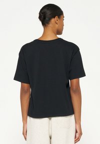 T-shirt nera a maniche corte in cotone, con una vestibilità comoda e scollo rotondo. Tessuto liscio con una finitura sottile.