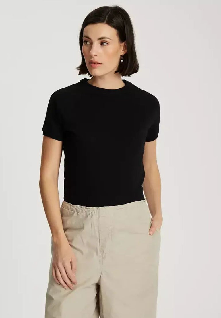 Czarny, krótki t-shirt z gładkiego materiału, z okrągłym dekoltem, w zestawie z jasnobeżowymi, luźnymi spodniami.