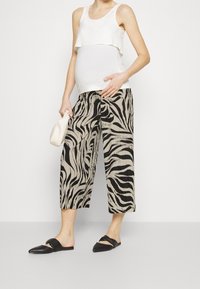 Vitt lager-topp i flera lager i kombination med svarta och beige zebrarandiga vida byxor och svarta slidesandaler, vilket skapar en kontrasterande monokrom look.