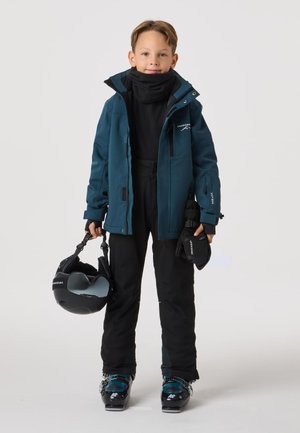 Lasketteluasu, jossa on turkoosi vedenpitävä takki, musta lämpöpaita, mustat housut, laskettelukypärä ja käsineet. Saappaat ovat mustat ja niissä on turkoosit yksityiskohdat.