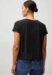 Sort kortærmet t-shirt med rund hals, lavet af glat stof. Har en afslappet pasform og en let buet kant, kombineret med blå jeans.