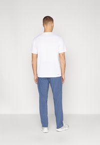T-shirt blanc à manches courtes associé à un pantalon bleu. Le T-shirt présente un col rond ; le pantalon a une coupe décontractée avec une texture lisse.