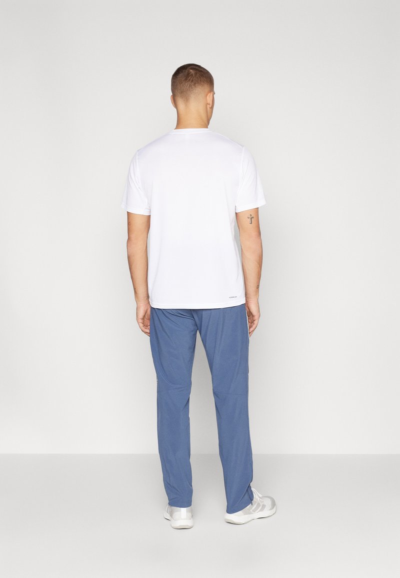 Weißes Kurzarm-T-Shirt kombiniert mit blauen Hosen. Das T-Shirt hat einen runden Ausschnitt; die Hose hat eine lockere Passform mit einer glatten Textur.