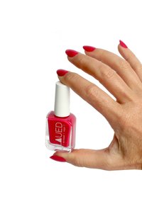 Smalto per unghie rosa brillante in una boccetta di vetro quadrata con un tappo bianco, tenuto tra le dita con una manicure rosa abbinata su unghie sottili.