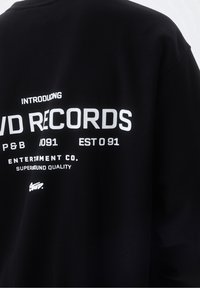 Černá mikina s bílým textem "PŘEDSTAVUJEME P&B 091 ZALOŽENO 091", s výrazným nápisem "LVD RECORDS". Měkká texturová tkanina.